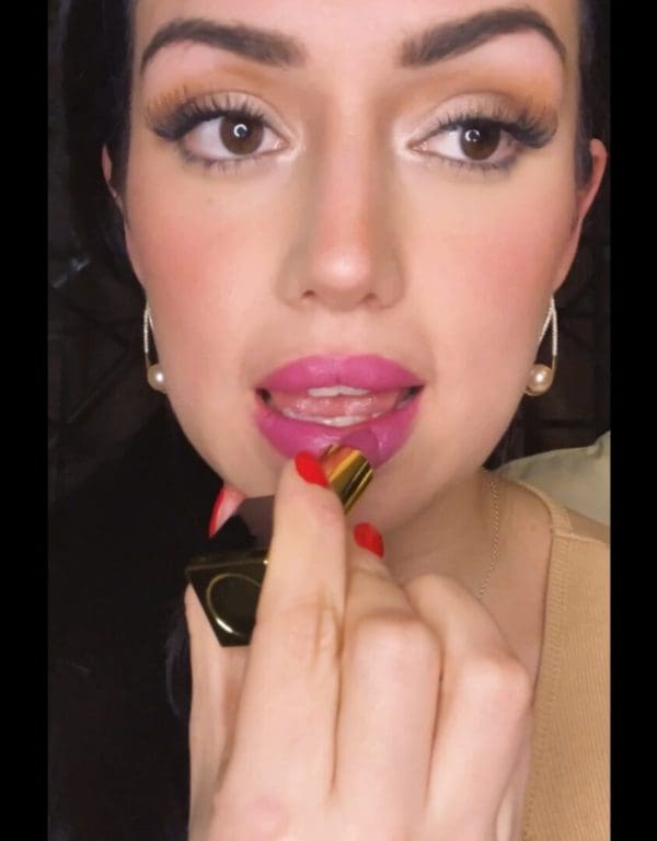 A woman putting lipstick on her lips.