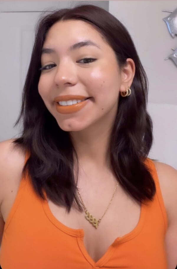 A woman in an orange top smiling for the camera.