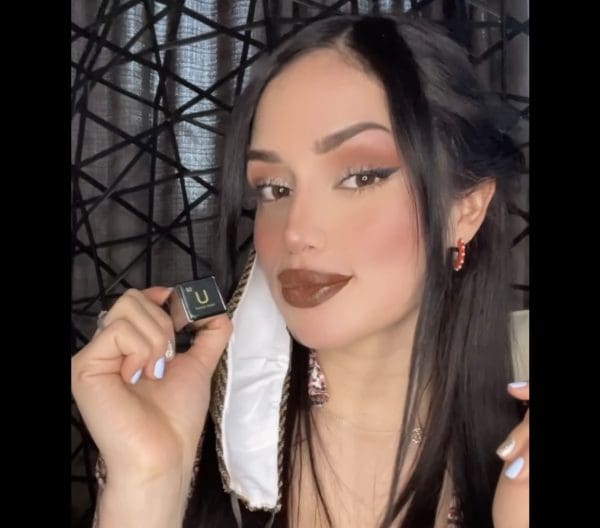 A woman with dark hair and brown lipstick holding a brush.