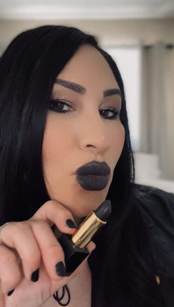 A woman with black lipstick holding a gold tube.