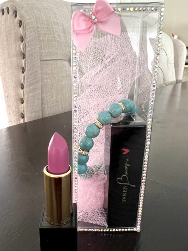 A pink lipstick and blue bracelet on top of a table.