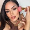 A woman is holding a makeup brush and posing for the camera.