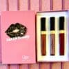 Three lipsticks in a box on top of a pink table.